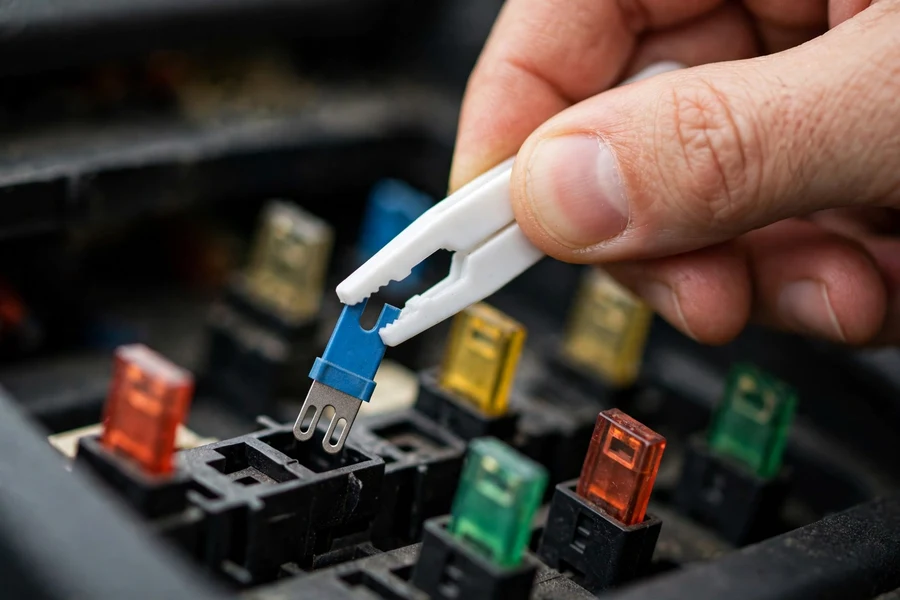 Hand using a white plastic fuse puller to remove a blue blade fuse from a car fuse panel
