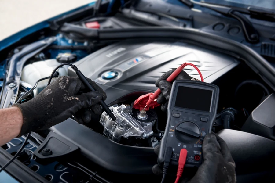 Mechanic testing battery voltage with a digital multimeter in a BMW engine bay