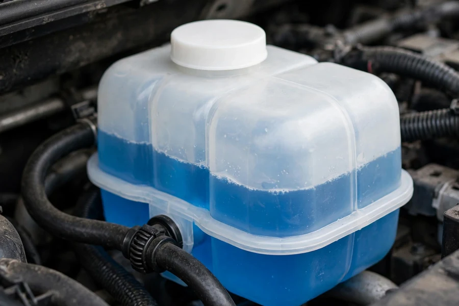 Translucent coolant expansion tank filled with blue coolant in a BMW engine bay, plain white filler cap