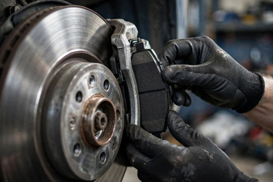 Gloved hands fitting a new brake pad into a BMW 3 Series front brake caliper next to the brake disc