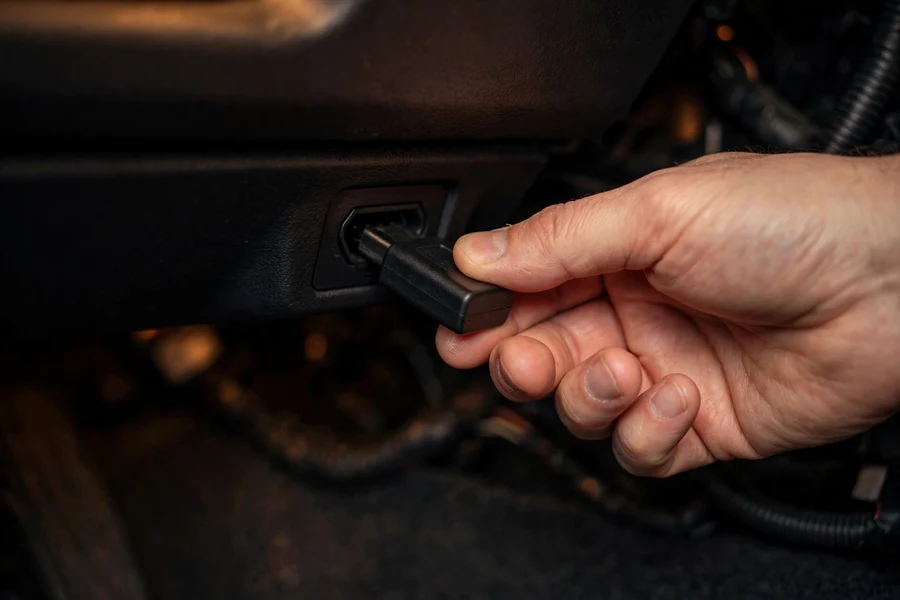 Hand plugging an OBD-II flash adapter into a BMW's diagnostic port under the dashboard
