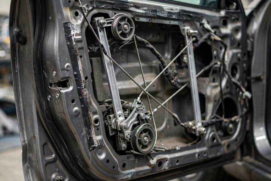 Close-up of a BMW door with the interior trim panel removed, showing the window regulator cable mechanism and guide rails