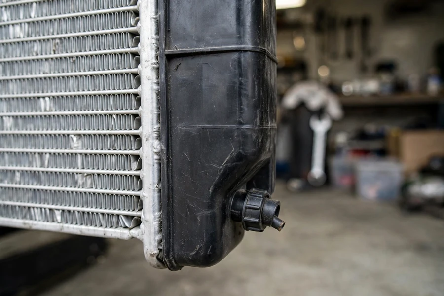 Close-up of a car radiator drain petcock on the lower plastic end tank beside the aluminum cooling fins