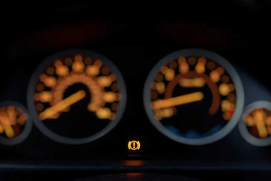 BMW 3 Series instrument cluster at night with an amber parking brake warning light illuminated