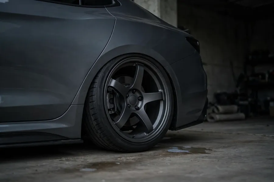 Rear wheel of a gray sports sedan sitting flush with the fender in a garage