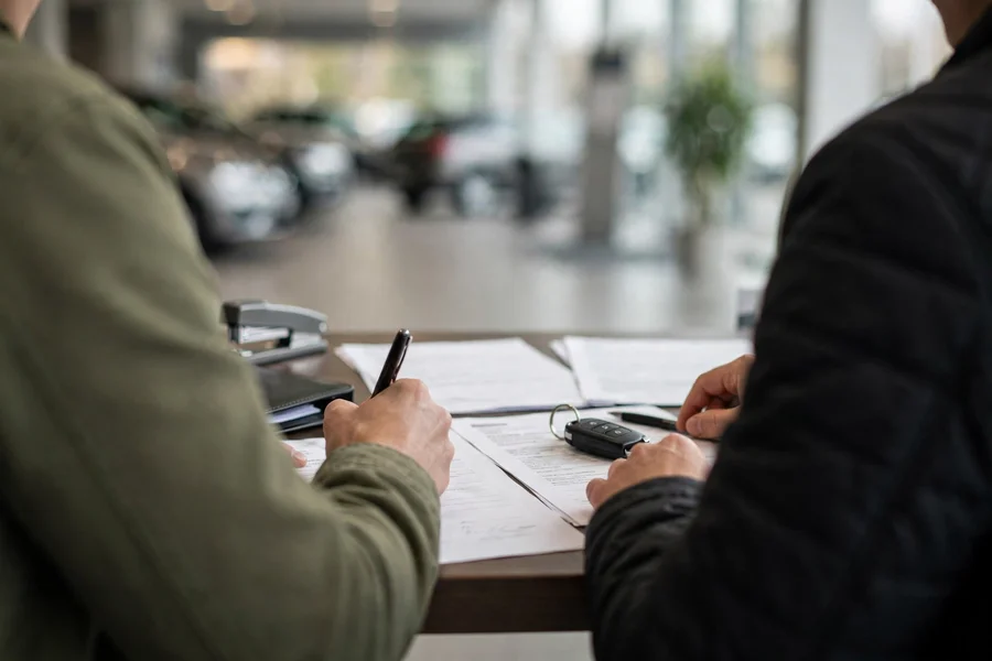 Two people shaking hands over a car purchase agreement at a dealership desk