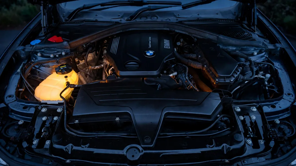 BMW 3 Series engine bay at dusk with the coolant expansion tank glowing amber